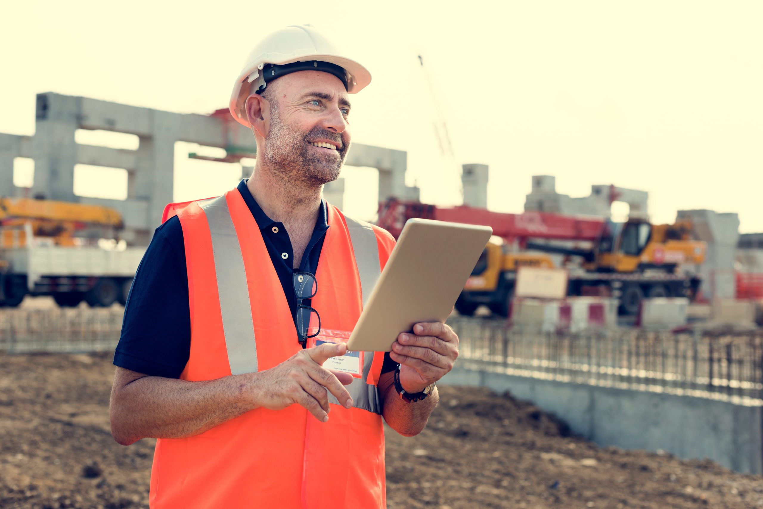 Construction site manager using a plant inspection app on tablet with heavy plant machinery in the background