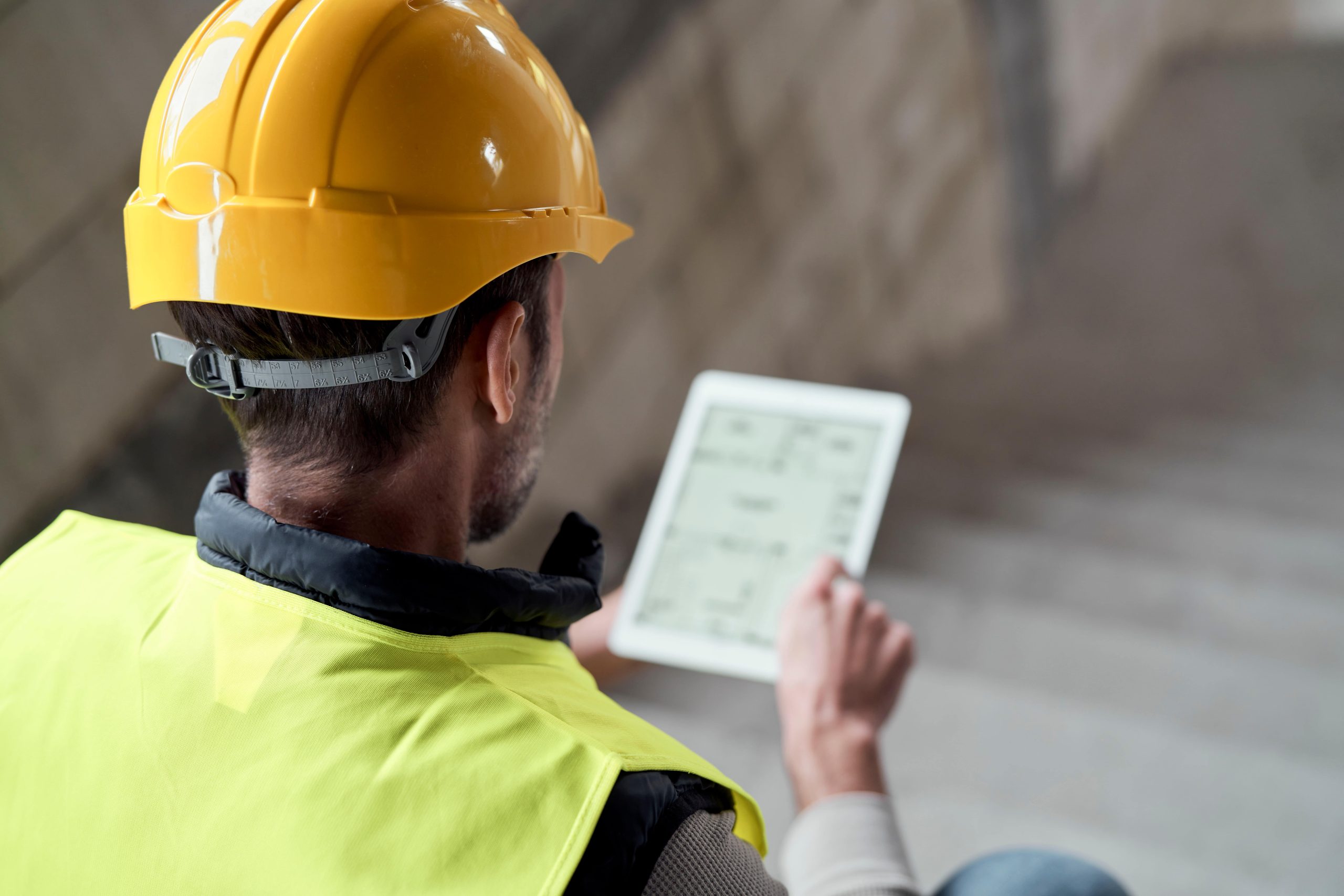 Construction worker in hi-vis vest and hard hat using a tablet to complete a digital preuse inspection on site