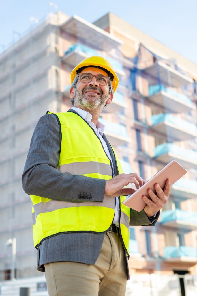 Construction site manager in hi-vis and hard hat reviewing CDM Regulations 2015 compliance documents on a tablet