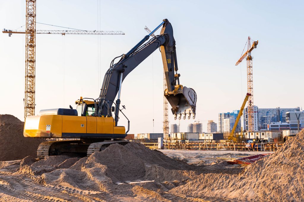 Yellow excavator operating on active construction site — heavy plant equipment subject to pre-use inspection requirements under PUWER