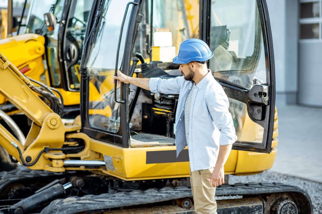 Operator in a hard hat carrying out a pre-use inspection of an excavator on a construction site
