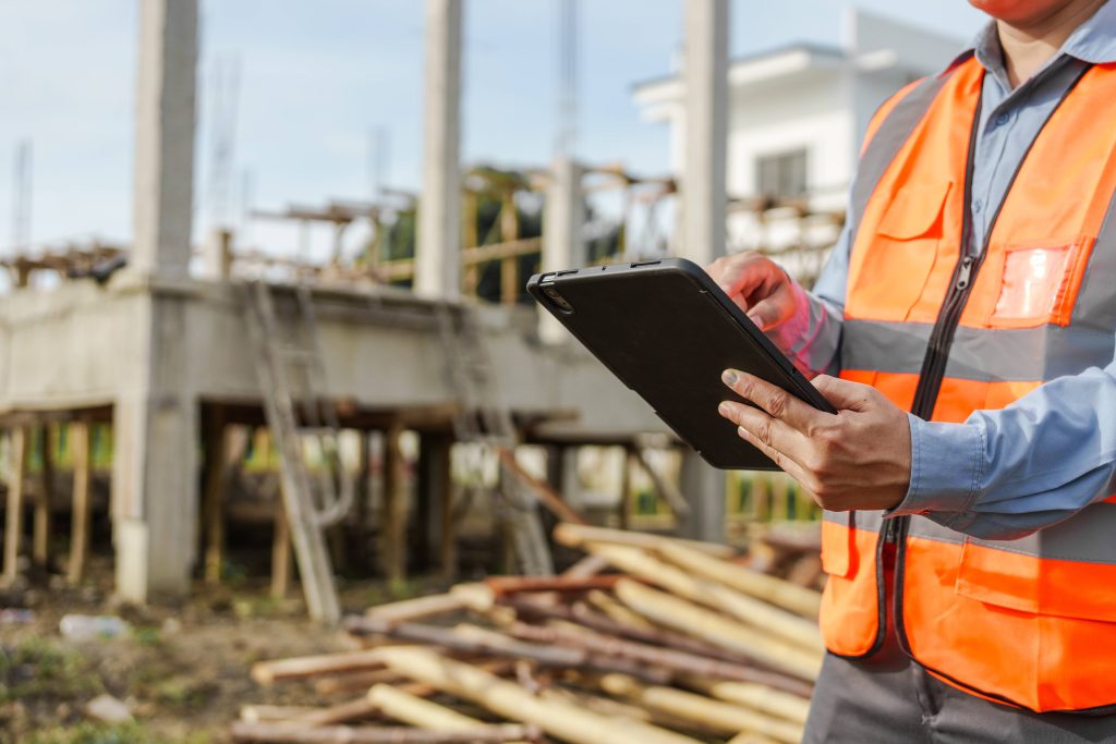 Site manager in a hi-vis vest reviewing digital inspection records on a tablet at a construction site