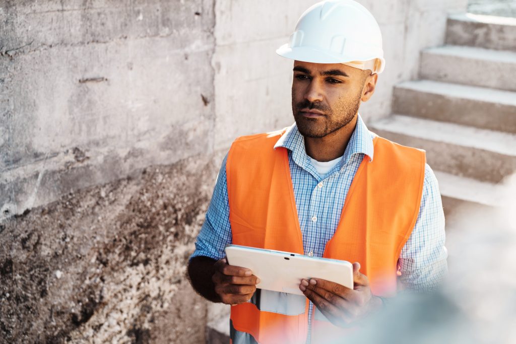 Site worker recording a plant inspection on a tablet in hi-vis and hard hat