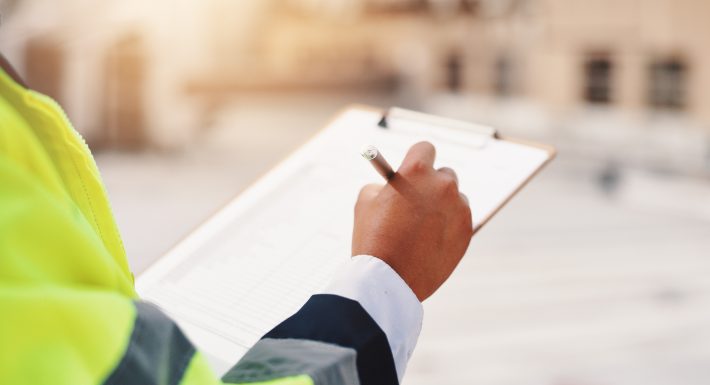 Construction worker in a hi-vis jacket completing a site safety inspection checklist on a clipboard