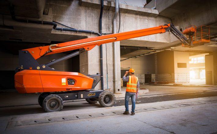 Operator carrying out a MEWP pre-use inspection on a boom lift before use on a construction site